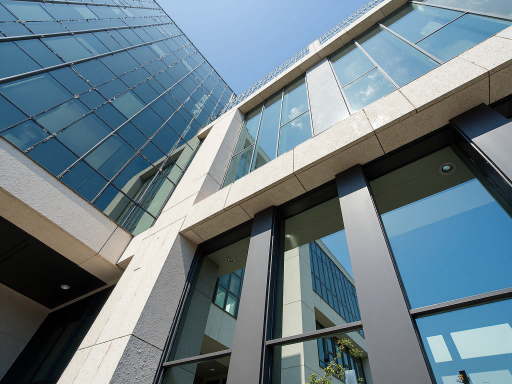 现代化办公大楼外景，玻璃幕墙设计，阳光照射下呈现科技感，周围绿植环绕